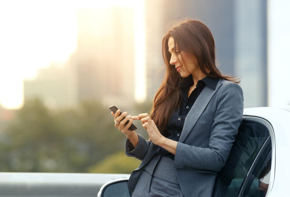 Woman leaning on car and typing into phone
